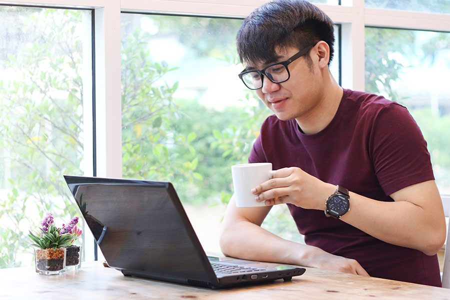 Report A Claim - Young Man Drinking Coffee And Working On His Laptop At Home