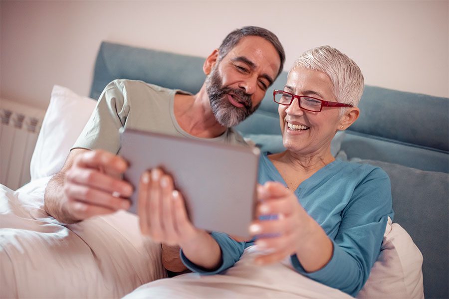 Request Policy Change - Smiling Mature Couple Sitting At Home Using Their Laptop